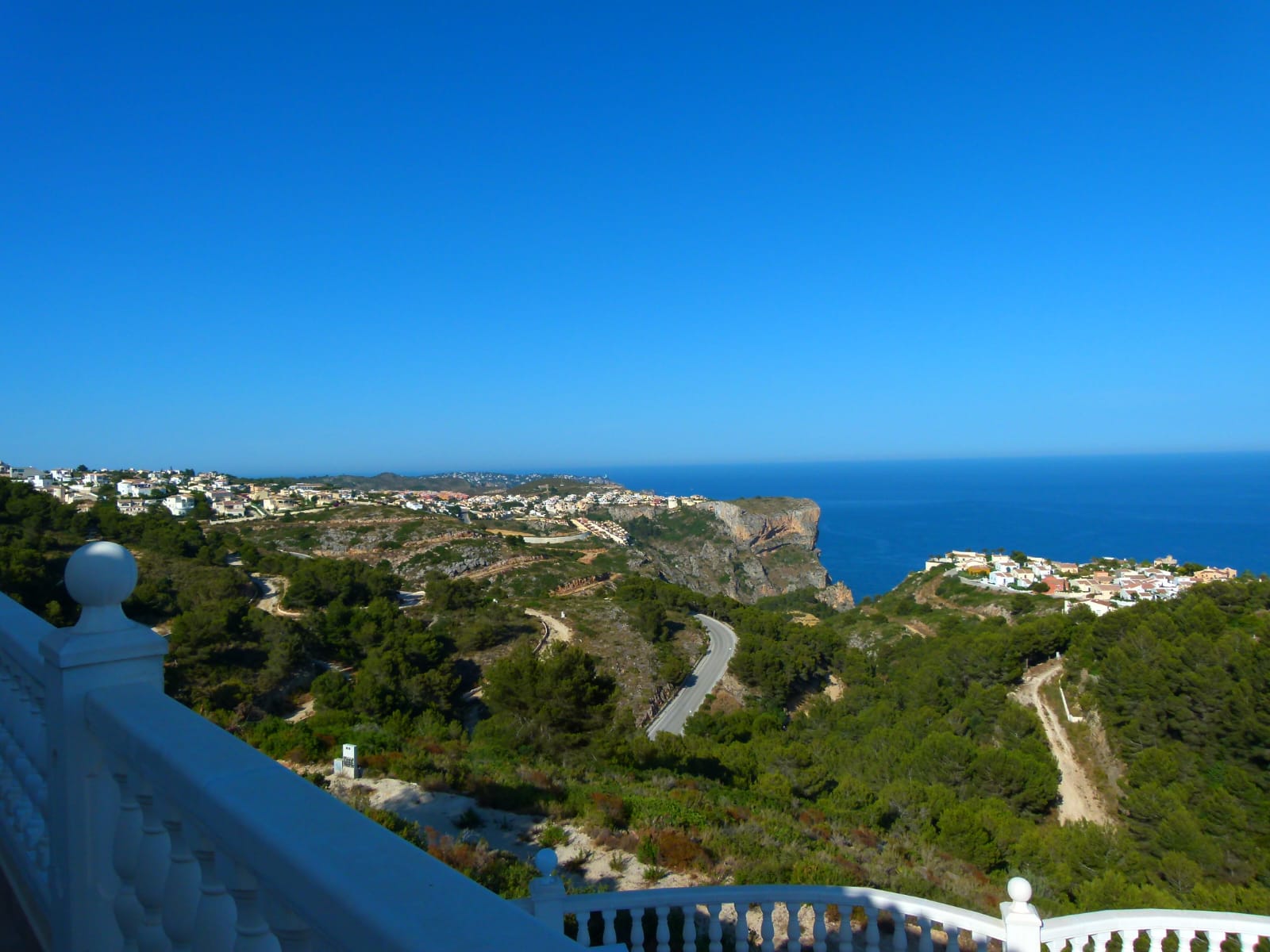 Panoramablick von der Terrasse mit weißem Geländer auf die Küste und das blaue Meer.