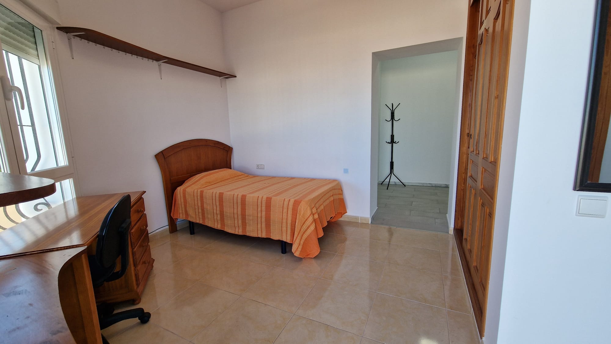 Schlafzimmer mit Einzelbett, Holzschreibtisch und Einbauschrank.