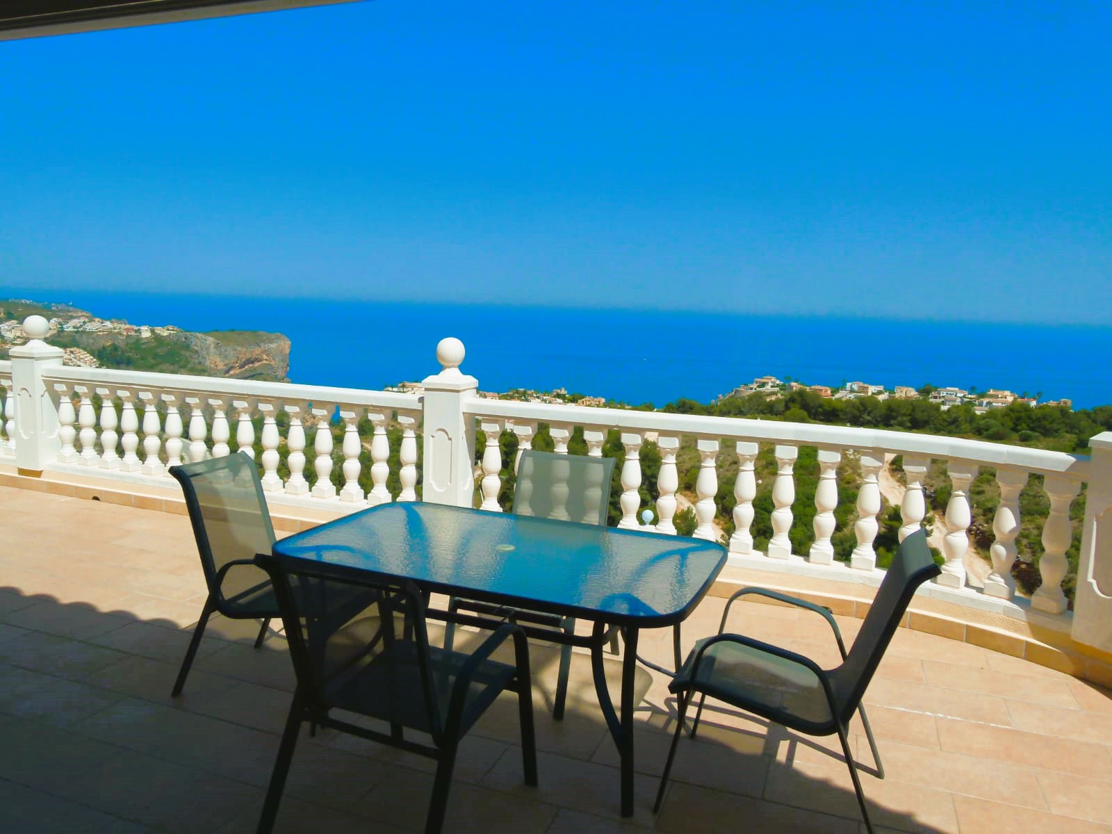 Terrasse mit Glastisch und Meerblick in Cumbre del Sol. Weißes Geländer mit Balustraden.