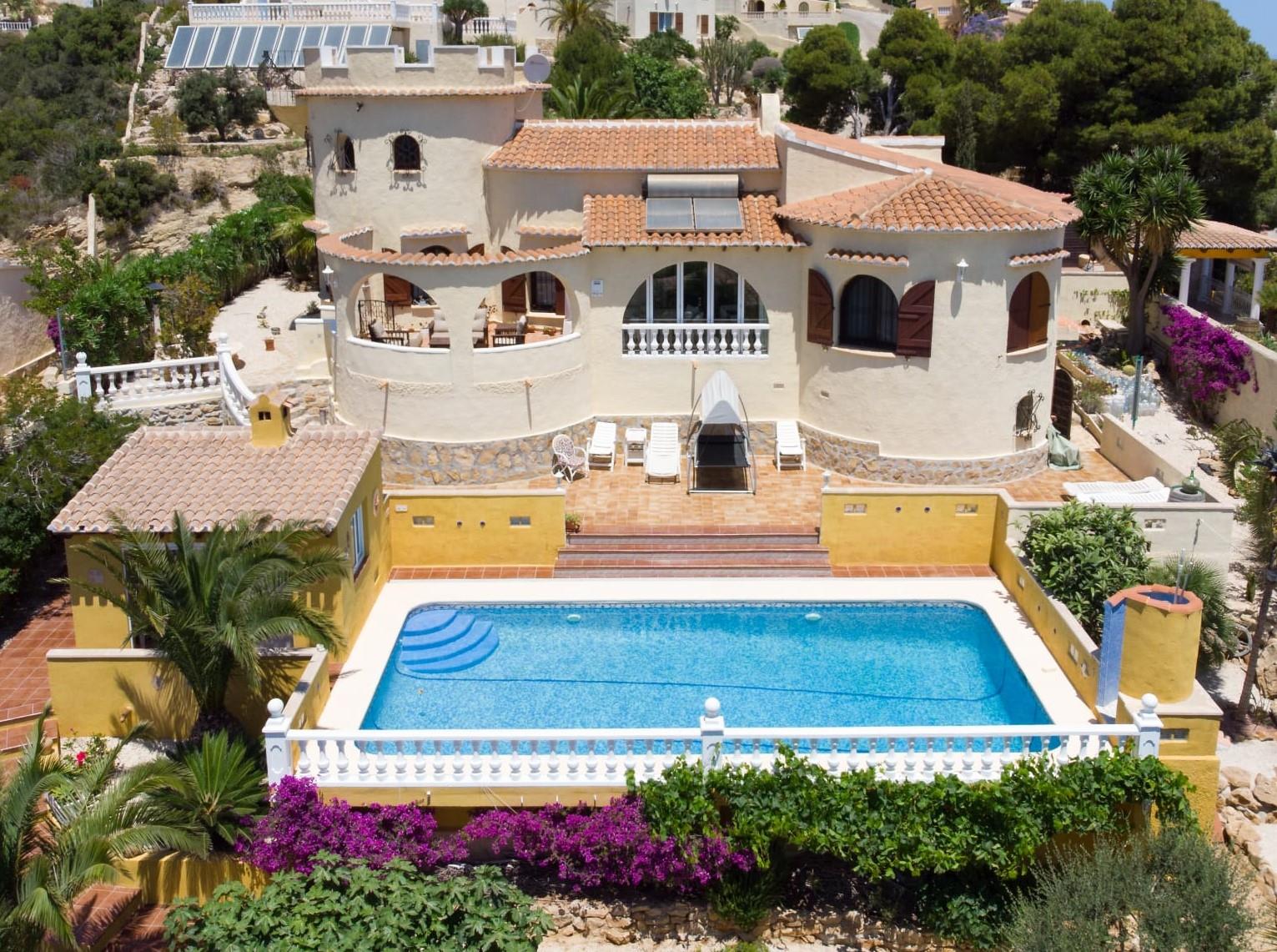 Außenansicht der Villa mit rechteckigem Pool, traditioneller Turmarchitektur, Terrakottadächern und einem mediterranen Garten mit Bougainvillea.