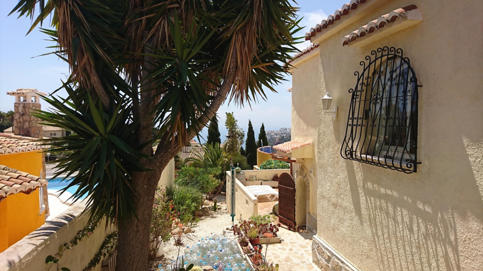 Außenansicht der Villa mit strukturierter Fassade, traditionellem schmiedeeisernem Fenstergitter und mediterranem Garten mit Blick auf das Meer.