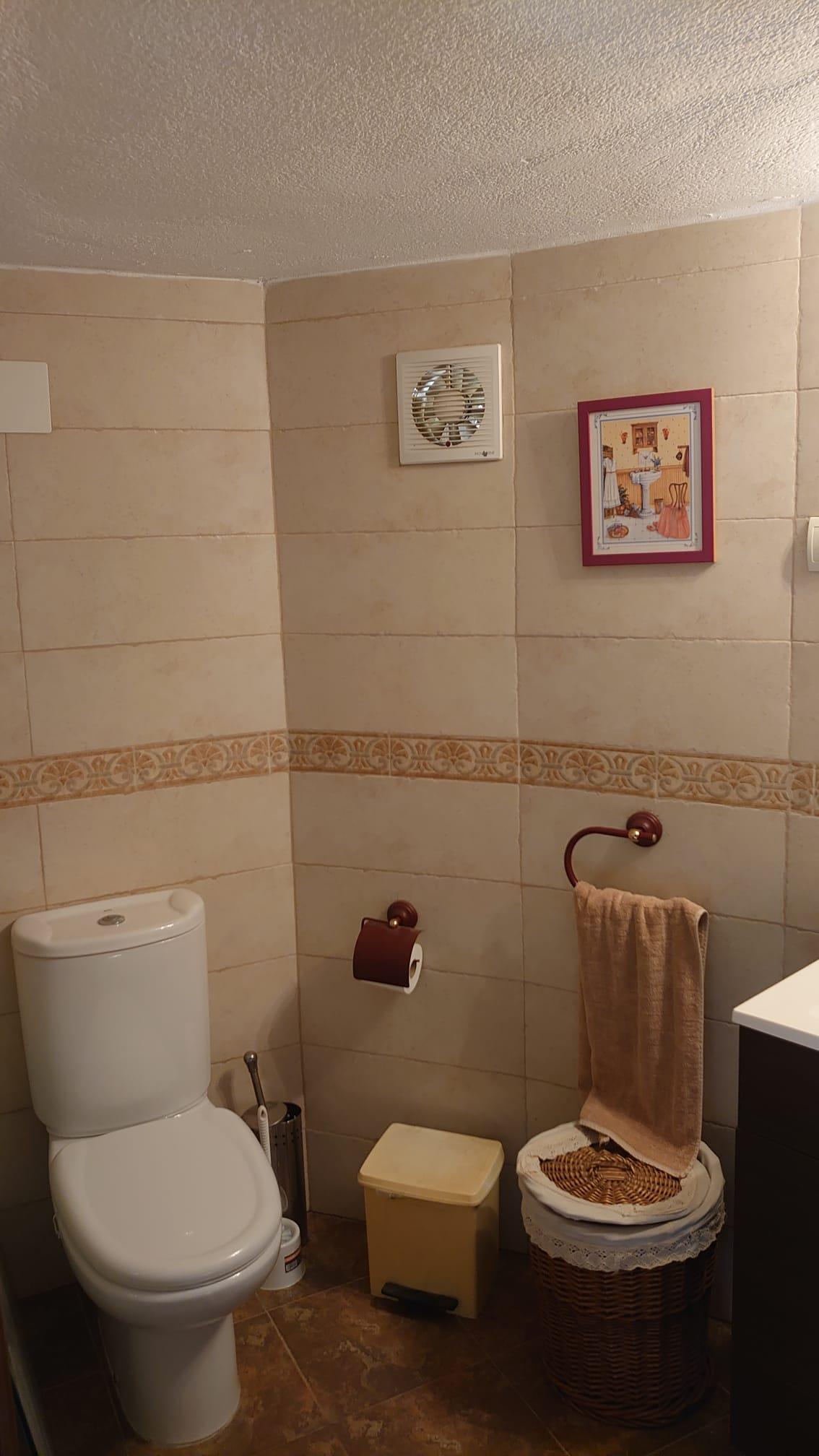 Badezimmer mit cremefarbenen Wandfliesen und dekorativer Bordüre. Ausgestattet mit weißem Keramik-WC, Holzzubehör und einem geflochtenen Wäschekorb.