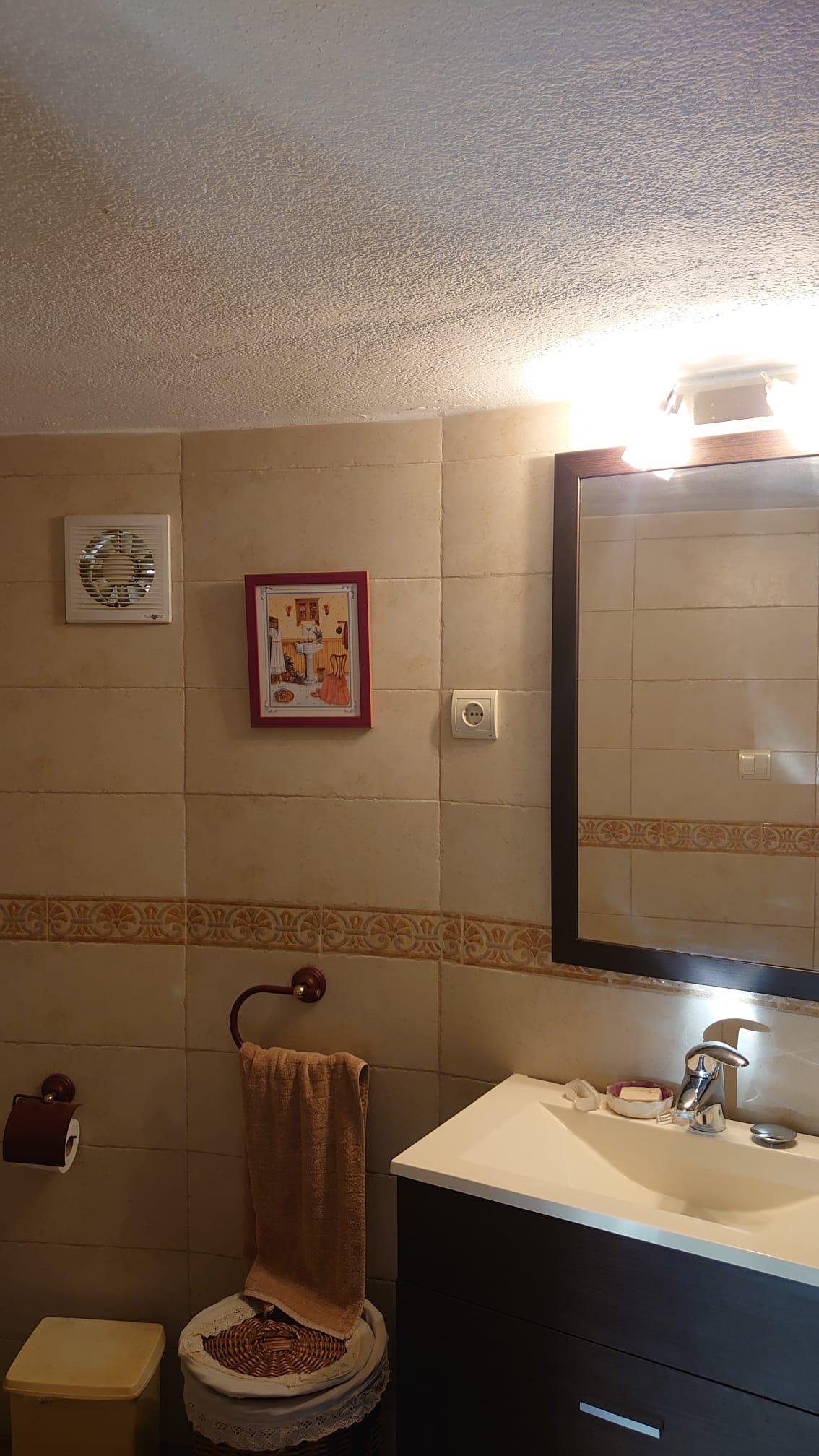 Badezimmer mit dunklem Waschtisch, integriertem Waschbecken, gerahmtem Spiegel mit Beleuchtung und beigefarbenen Fliesen mit dekorativer Bordüre.
