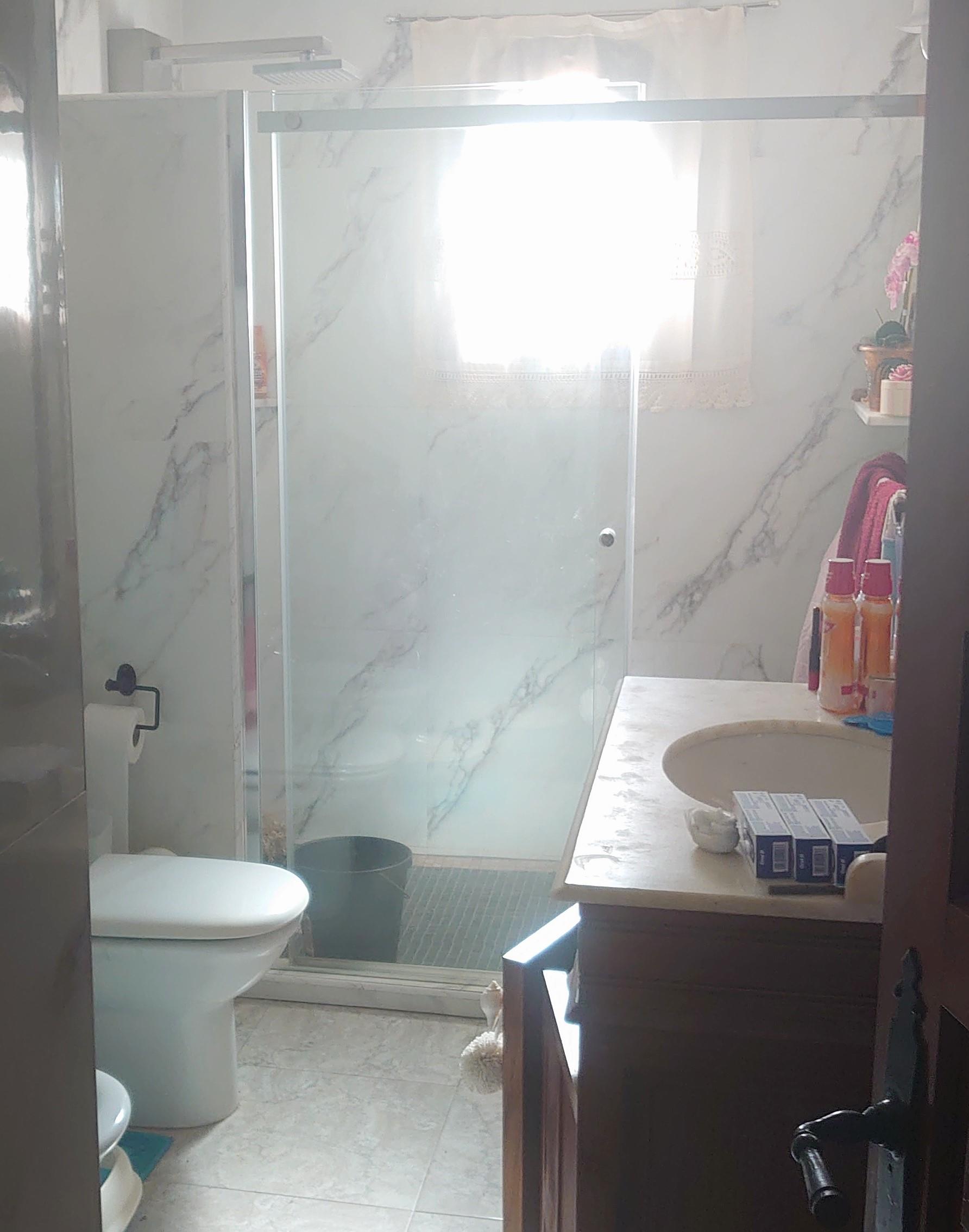 Badezimmer mit ebenerdiger Dusche, Marmoroptik-Fliesen und Glasschiebetür. Ein Holzwaschtisch mit Natursteinplatte ergänzt das helle Design.