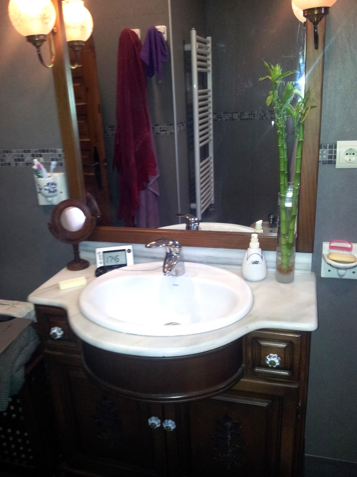 Badezimmer mit weißer Marmorplatte, eingelassenem Waschbecken, dunklem Holzunterschrank mit Keramikknöpfen und einem großen Spiegel mit klassischen Wandleuchten.