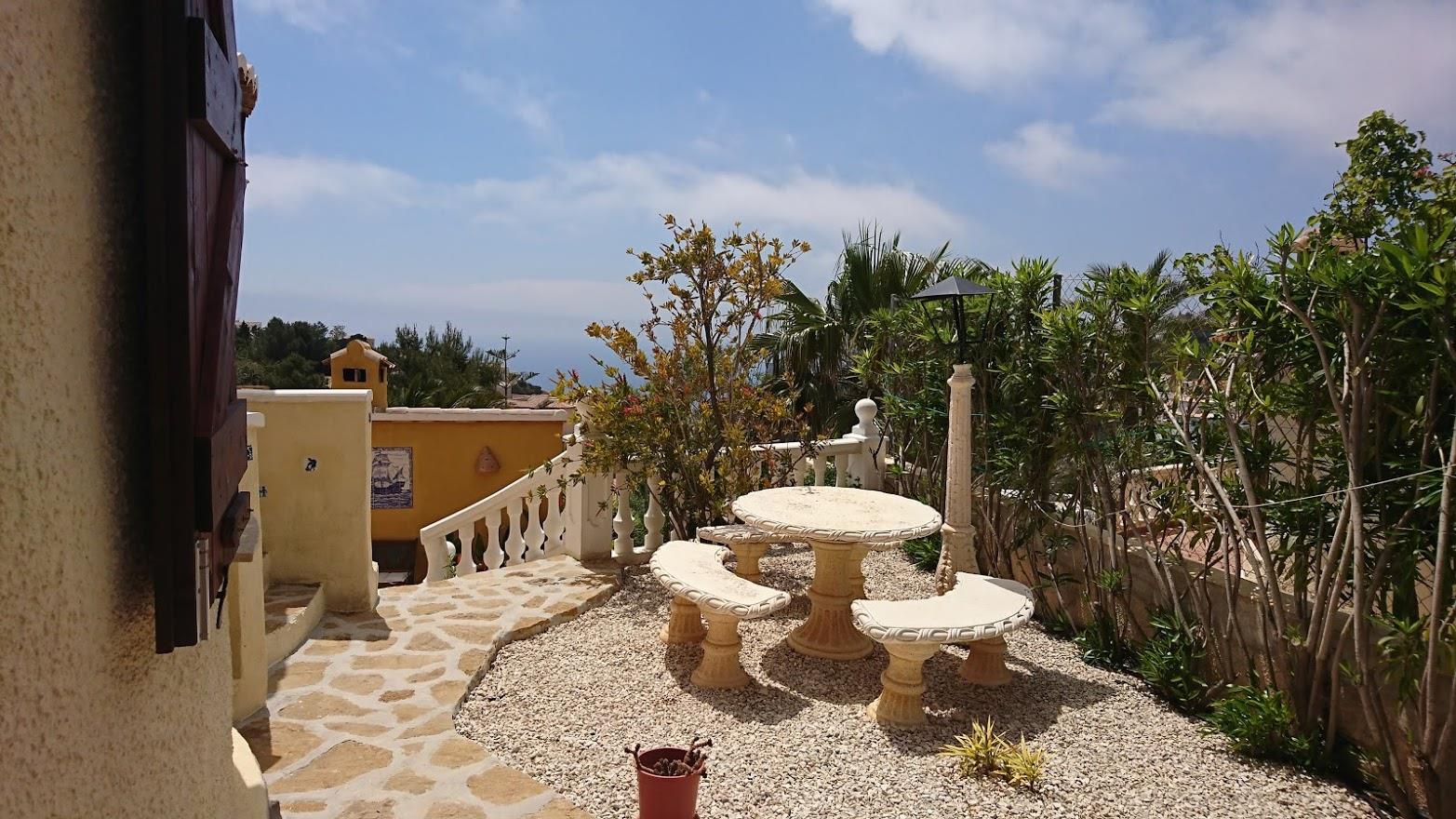 Kiesterrasse mit Sitzgruppe aus Naturstein, eingefasst von einer weißen Balustrade und mediterranen Pflanzen mit Blick auf das Meer.