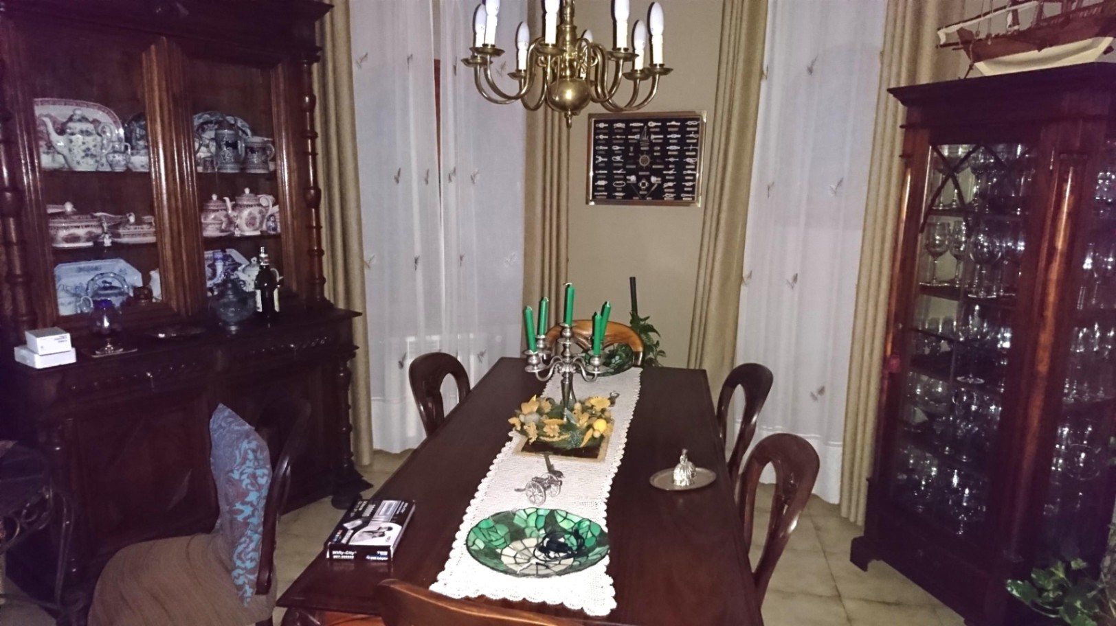Klassisches Esszimmer mit Massivholztisch, verzierten Vitrinenschränken für Geschirr und einem Messing-Kronleuchter über einem Spitzen-Tischläufer.