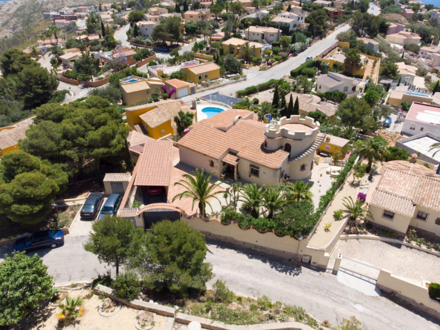 Luftaufnahme der mediterranen Villa mit markantem Zinnenturm, Terrakotta-Ziegeldach und einem privaten Garten mit ausgewachsenen Palmen.