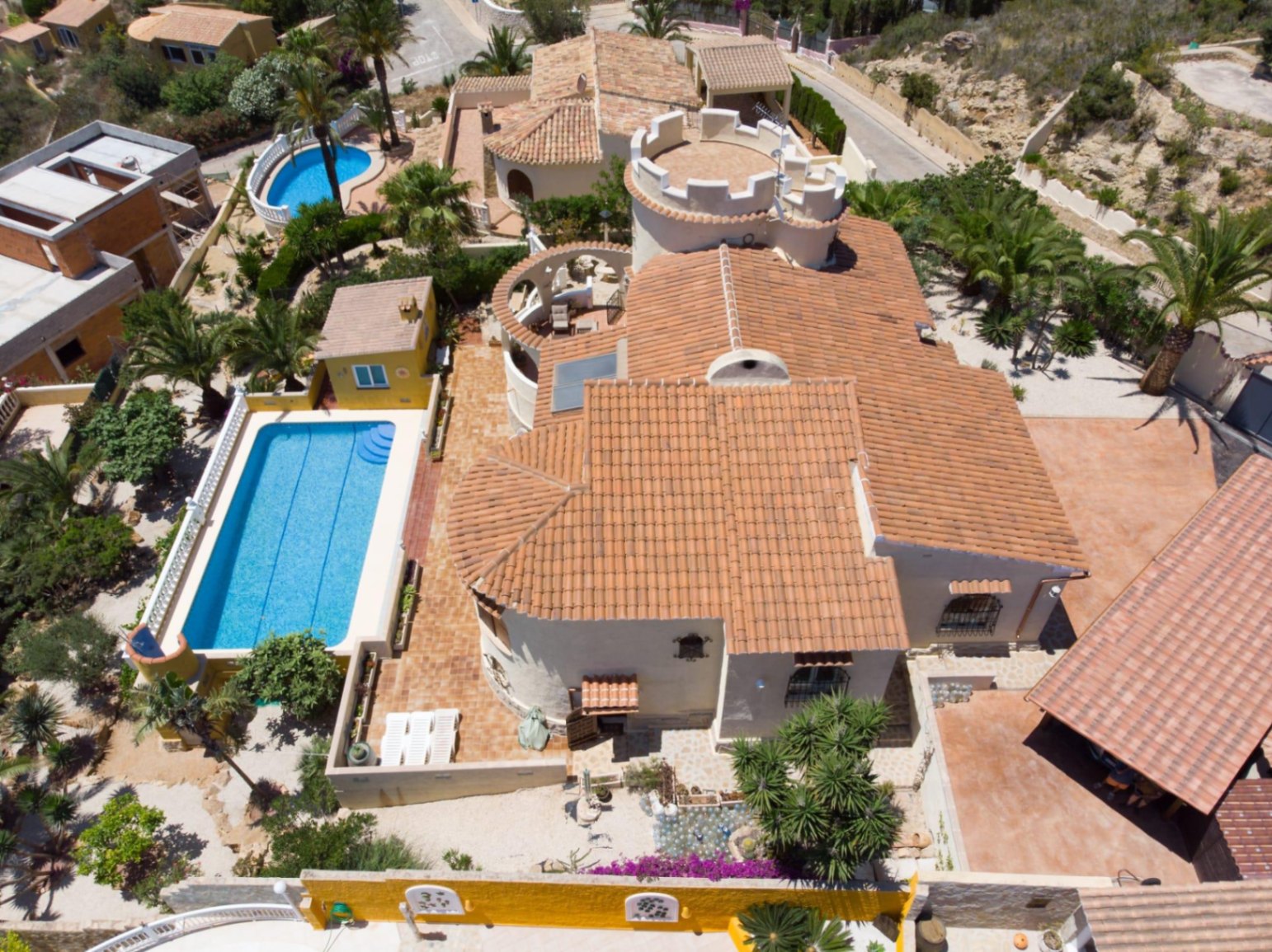 Luftaufnahme der Villa mit mediterraner Architektur, Terrakottadächern, einem markanten Zinnenturm und einem rechteckigen Pool inmitten gepflegter Außenanlagen.