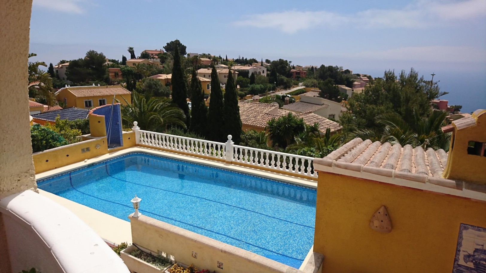 Rechteckiger 10x4 m Pool mit blauen Mosaikfliesen, weißer Balustrade und weitem Blick über die Wohngegend bis hin zum Mittelmeer.
