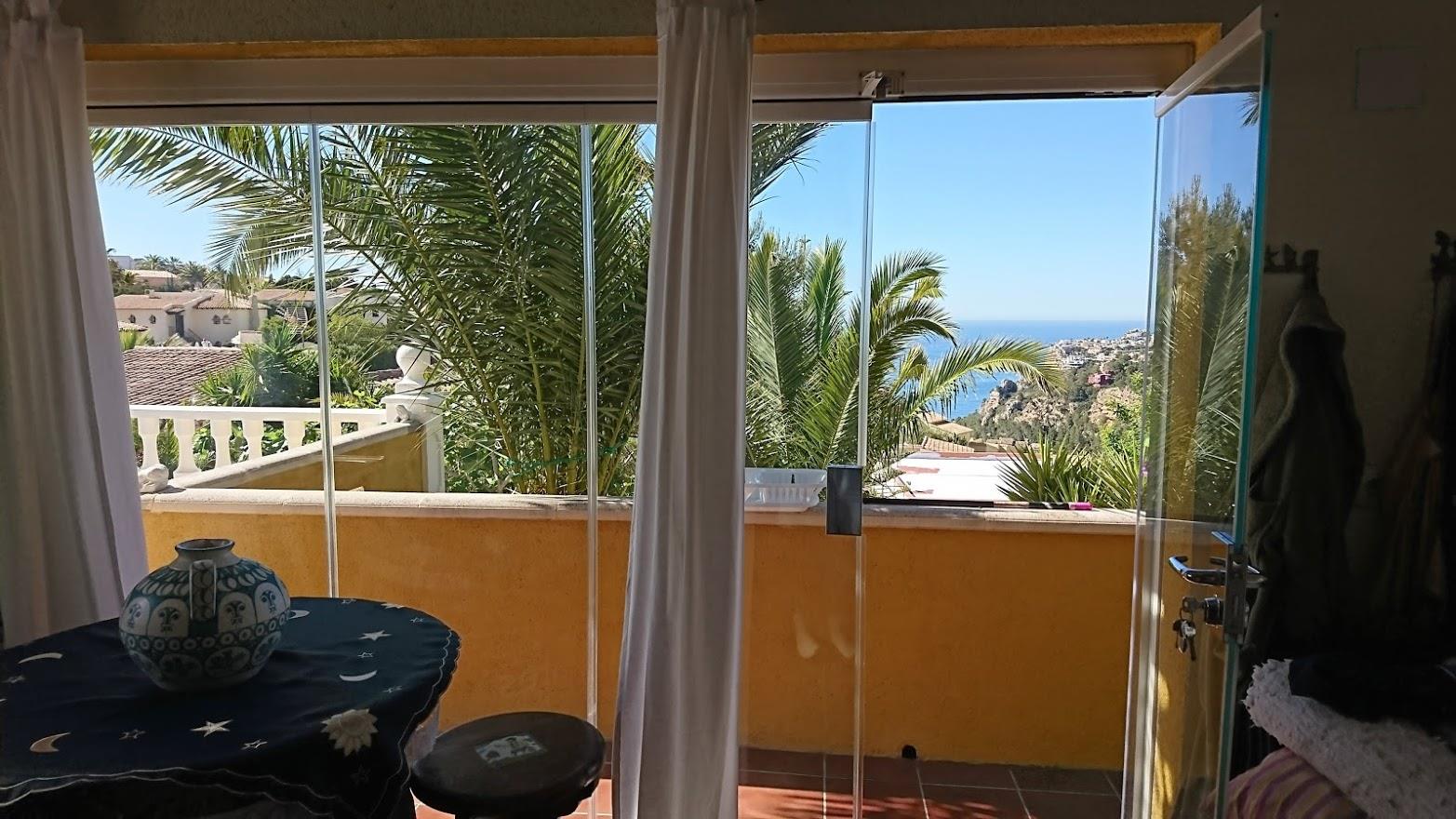 Verglaste Naya mit Blick auf das Meer und mediterrane Palmen. Die Glasschiebewände verbinden den Innenraum mit der Terrasse und lassen viel Tageslicht herein.