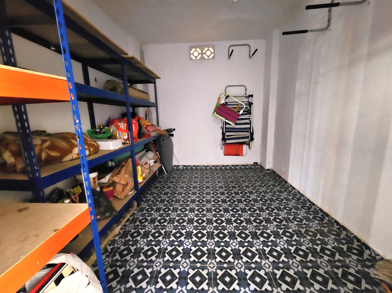 12 m² großer Abstellraum mit robusten Metallregalen, geometrisch gemustertem Fliesenboden und Wandhaken für die Organisation.