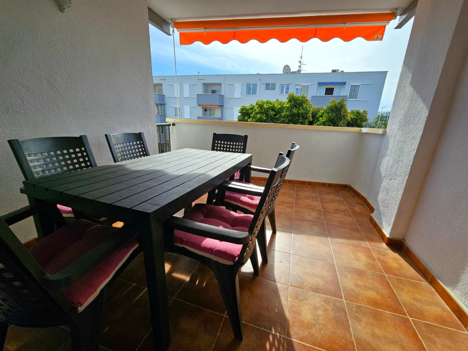 Außen-Terrasse mit Fliesenboden in Terrakotta-Optik, Essgruppe für sechs Personen und einer ausziehbaren orangefarbenen Markise als Sonnenschutz.
