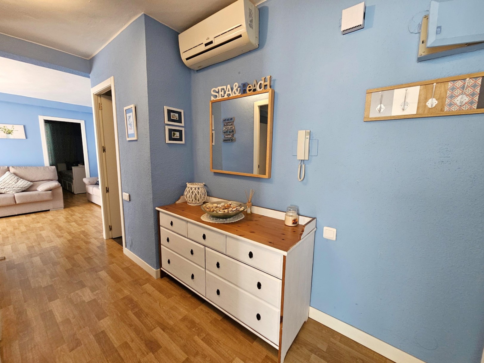 Eingangsbereich mit blauen Wänden, Parkettboden, einer weißen Holzkommode und Klimaanlage, der direkt in das Wohnzimmer und die Schlafzimmer führt.
