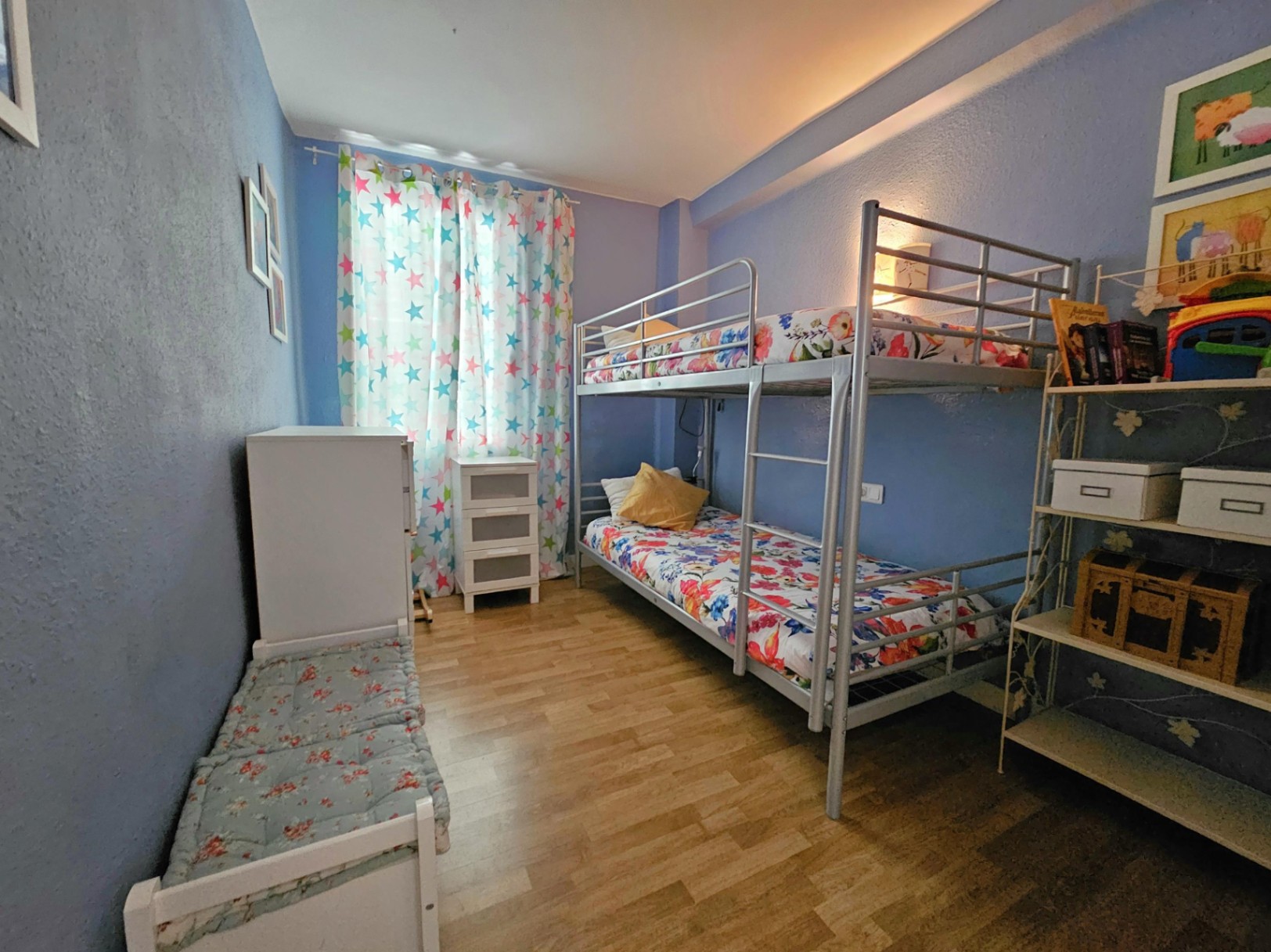 Kinderzimmer mit silbernen Metall-Etagenbetten, Parkettboden und blauen Wänden. Ausgestattet mit weißen Kommoden und funktionalen Regalen bei hellem Tageslicht.