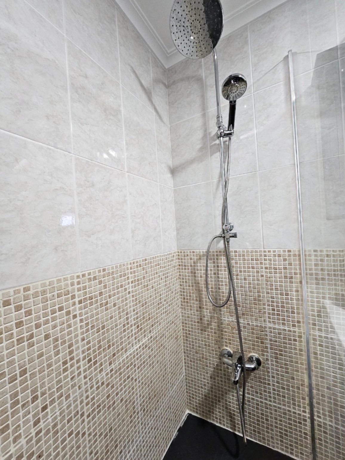 Moderne begehbare Dusche mit Doppel-Duschsystem, kombiniert mit erdfarbenen Mosaikfliesen und großformatigen Wandfliesen in Marmoroptik.