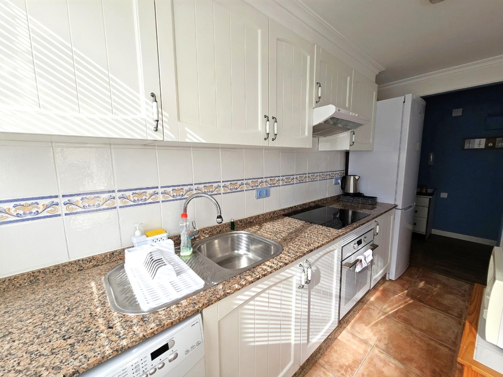 Renovierte Küche mit Granitarbeitsplatte, weißen Schränken im Landhausstil und dekorativem Fliesenspiegel. Ausgestattet mit Cerankochfeld und Backofen.
