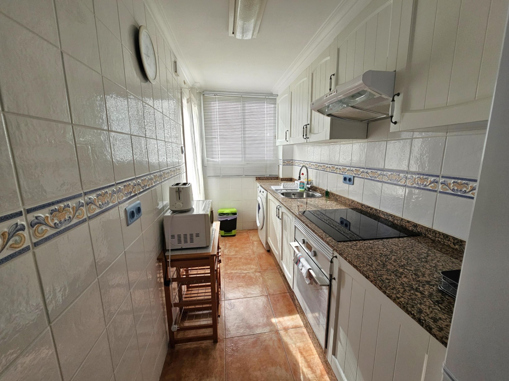 Renovierte Pantryküche mit Granitarbeitsplatte, weißen Fronten und integrierten Geräten. Das Fenster am Ende sorgt für eine helle Arbeitsatmosphäre.