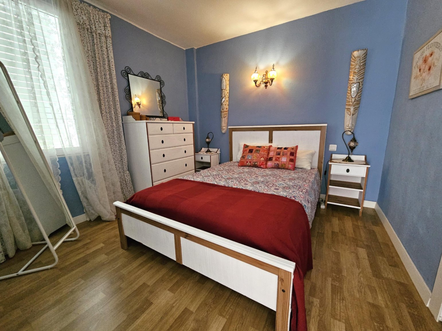 Zeitgenössisches Schlafzimmer mit blauen Wänden, Parkettboden und weißen Möbeln. Mit Doppelbett, Kommode und viel natürlichem Tageslicht.