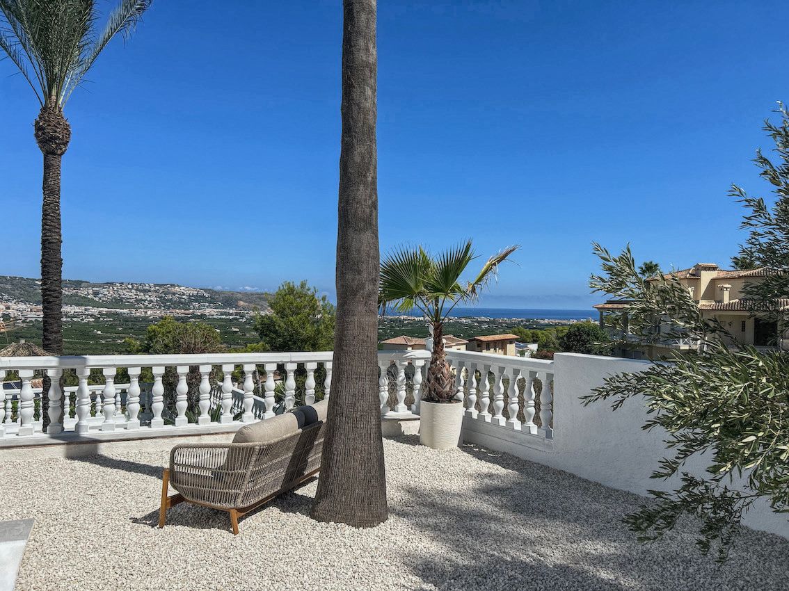 Außenanlage mit weißem Kies, modernen Loungemöbeln und klassischer Balustrade mit Panoramablick auf das Tal und das Mittelmeer.