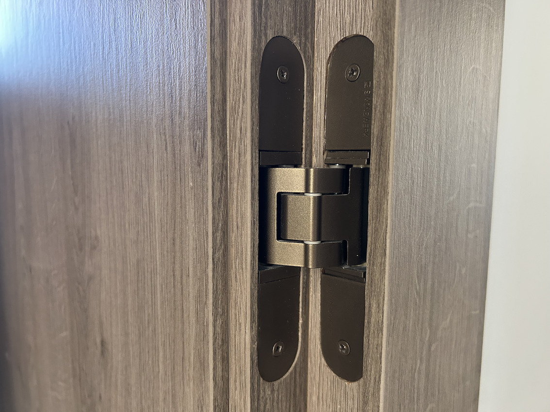 Detailansicht eines hochwertigen, verdeckt liegenden Türbands in Bronze-Optik, bündig eingelassen in dunkles Holzdekor für ein minimalistisches Design.