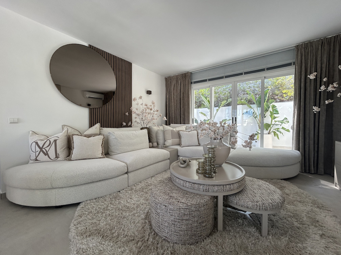 Moderner Wohnbereich mit geschwungenem Modulsofa, Akzentwand aus Holzlamellen mit Rundspiegel und großen Glasschiebetüren zur begrünten Terrasse.