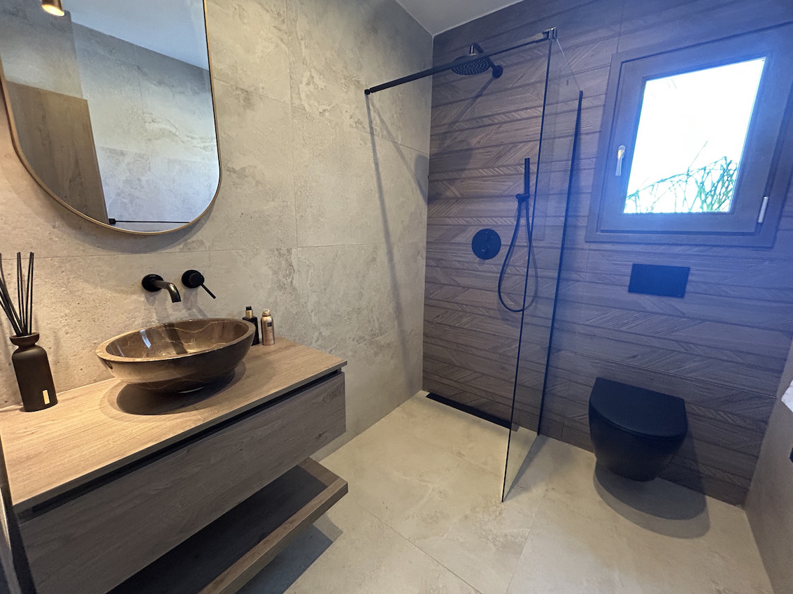 Modernes Badezimmer mit Steinwaschbecken auf Holzunterschrank, begehbarer Regendusche mit Glaswand und mattschwarzen Wand-WCs.