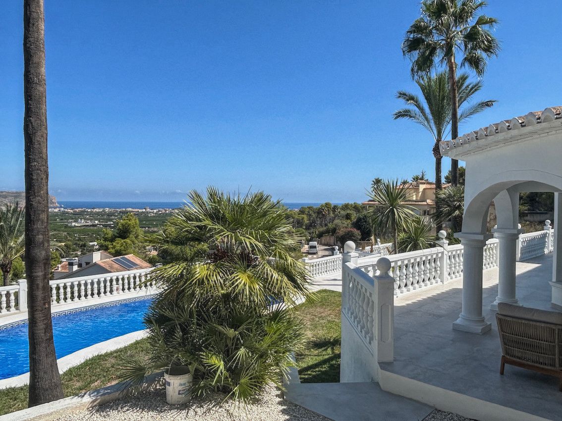 Terrasse mit weißen Balustraden und Rundbogen-Veranda mit Panoramablick auf das Meer und das Tal, umgeben von Palmen und dem Poolbereich.