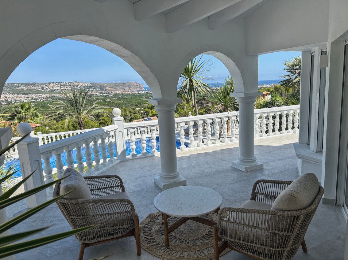 Überdachte Terrasse mit weißen Rundbögen, Rattan-Sitzgruppe und Panoramablick auf den Pool, das Tal und das Mittelmeer.