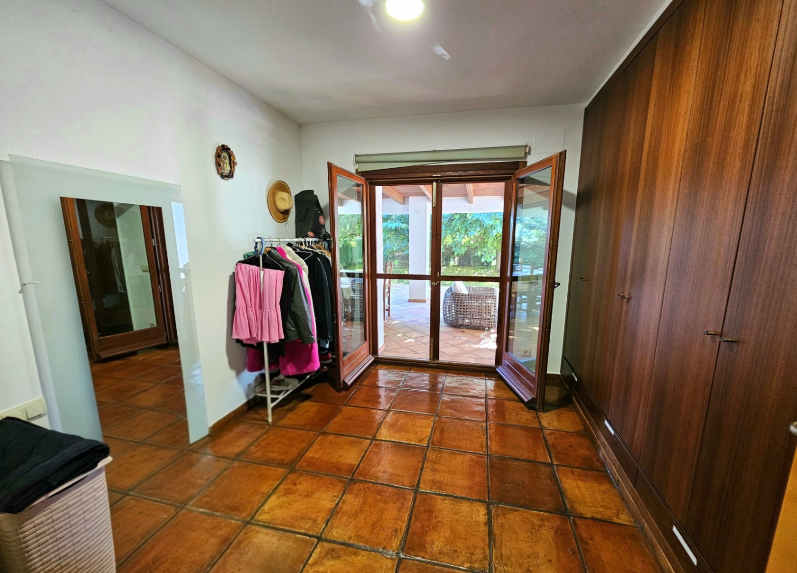 Ankleidezimmer mit großen Einbauschränken aus Holz, handgefertigten Tonfliesen und direktem Zugang zur überdachten Terrasse durch Glastüren.