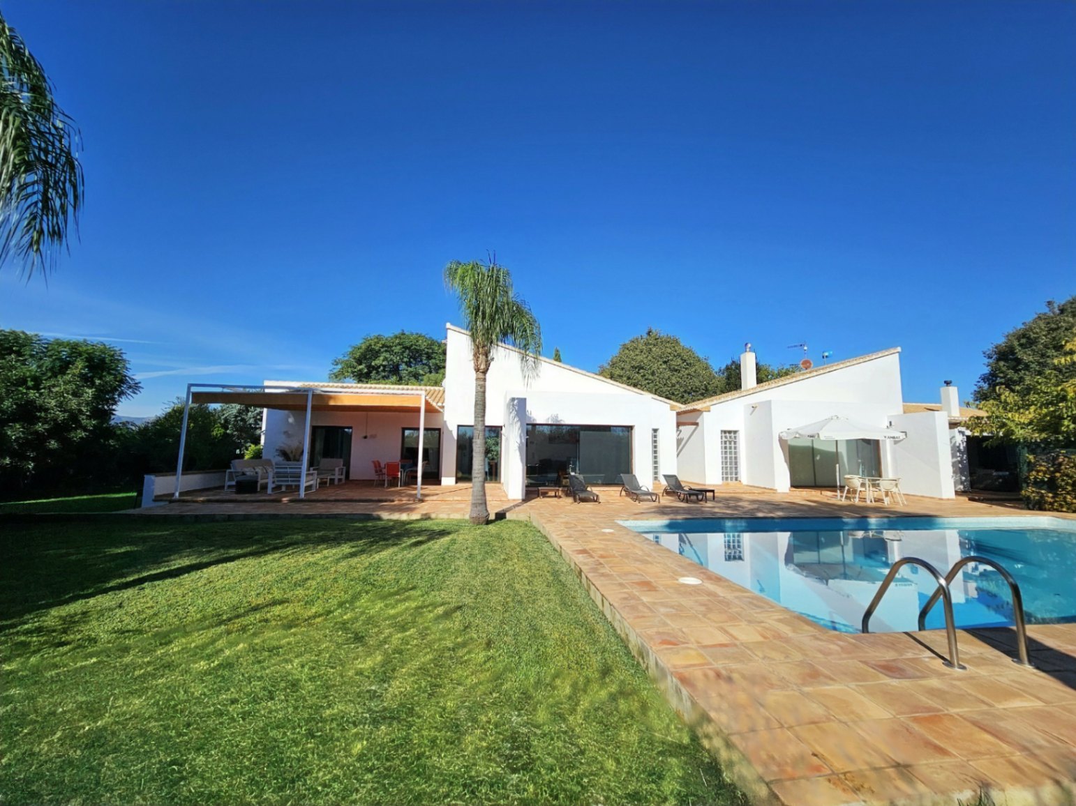 Außenansicht der Villa mit Pool, handgefertigten Tonfliesen, gepflegtem Rasen und einer überdachten Terrasse, die modernes Design und Privatsphäre vereint.