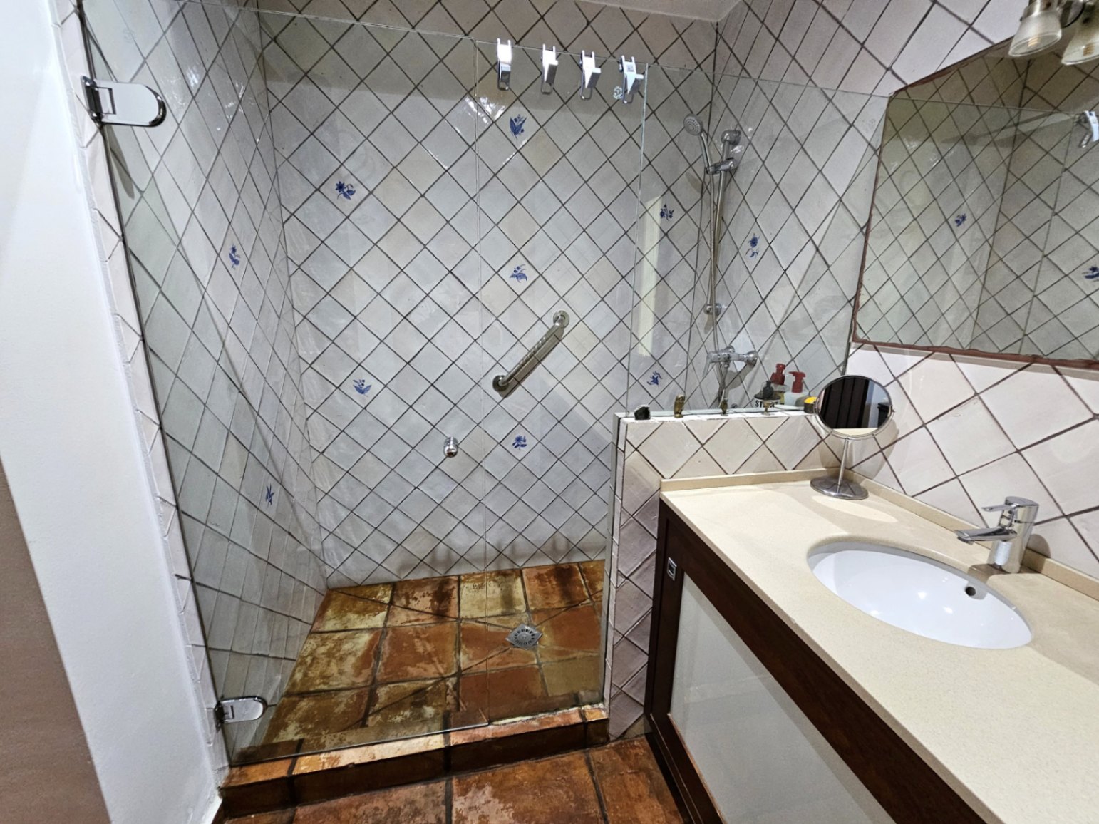 Badezimmer mit handbemalten Wandfliesen im Rautendesign, einer begehbaren Glasdusche und handgefertigten Tonfliesen am Boden.