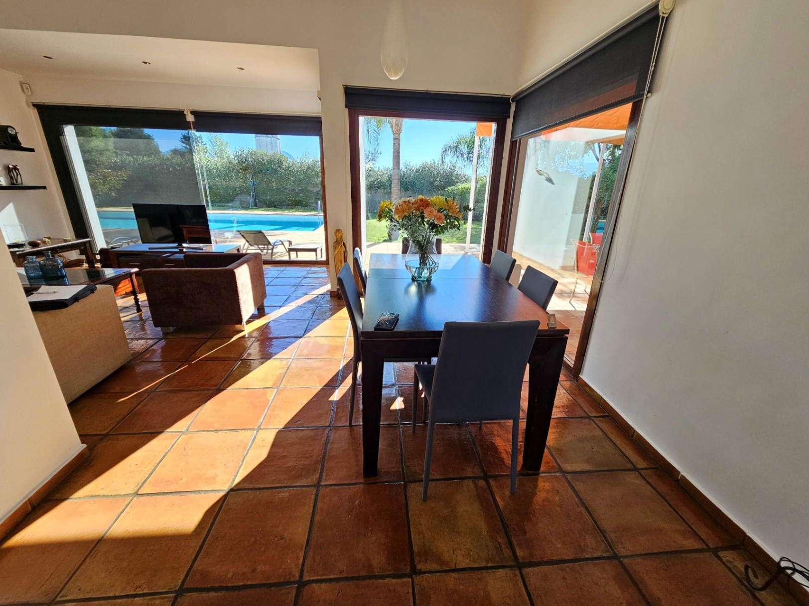 Essbereich mit handgefertigten Tonfliesen und großen Sicherheitsglasfenstern, die einen direkten Blick auf den Pool und Garten bieten.