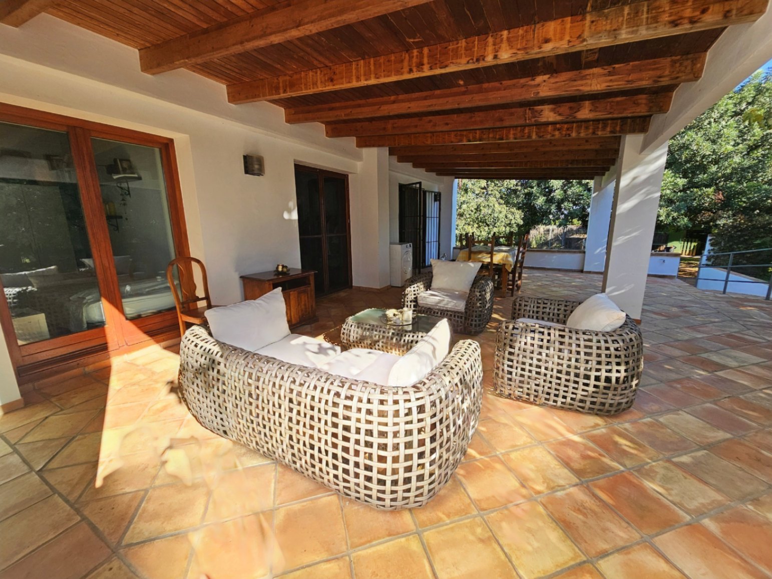 Großzügige überdachte Terrasse mit sichtbaren Holzbalken, handgefertigten Terrakottaböden und einer Rattan-Sitzgruppe mit Blick in den Garten.