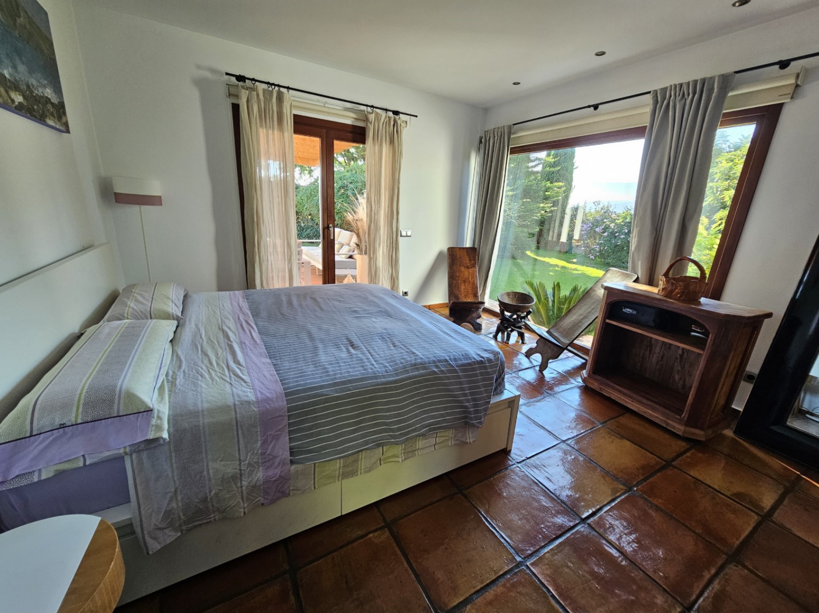 Helles Schlafzimmer mit handgefertigten Tonfliesen, direktem Zugang zum Garten und großen Fenstern, die viel natürliches Licht und Blick ins Grüne bieten.