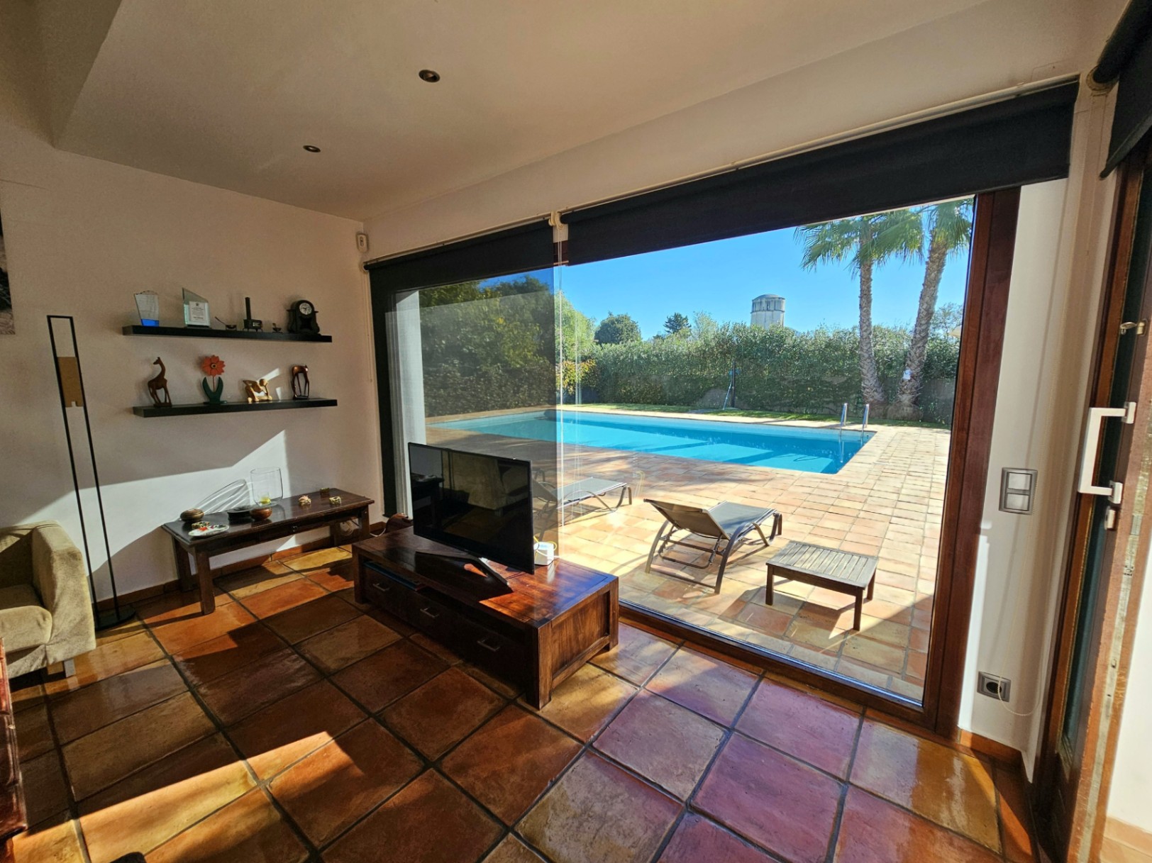 Wohnraum mit handgefertigten Tonfliesen und bodentiefen Glasfronten, die einen nahtlosen Übergang zur Terrasse und zum Pool schaffen.