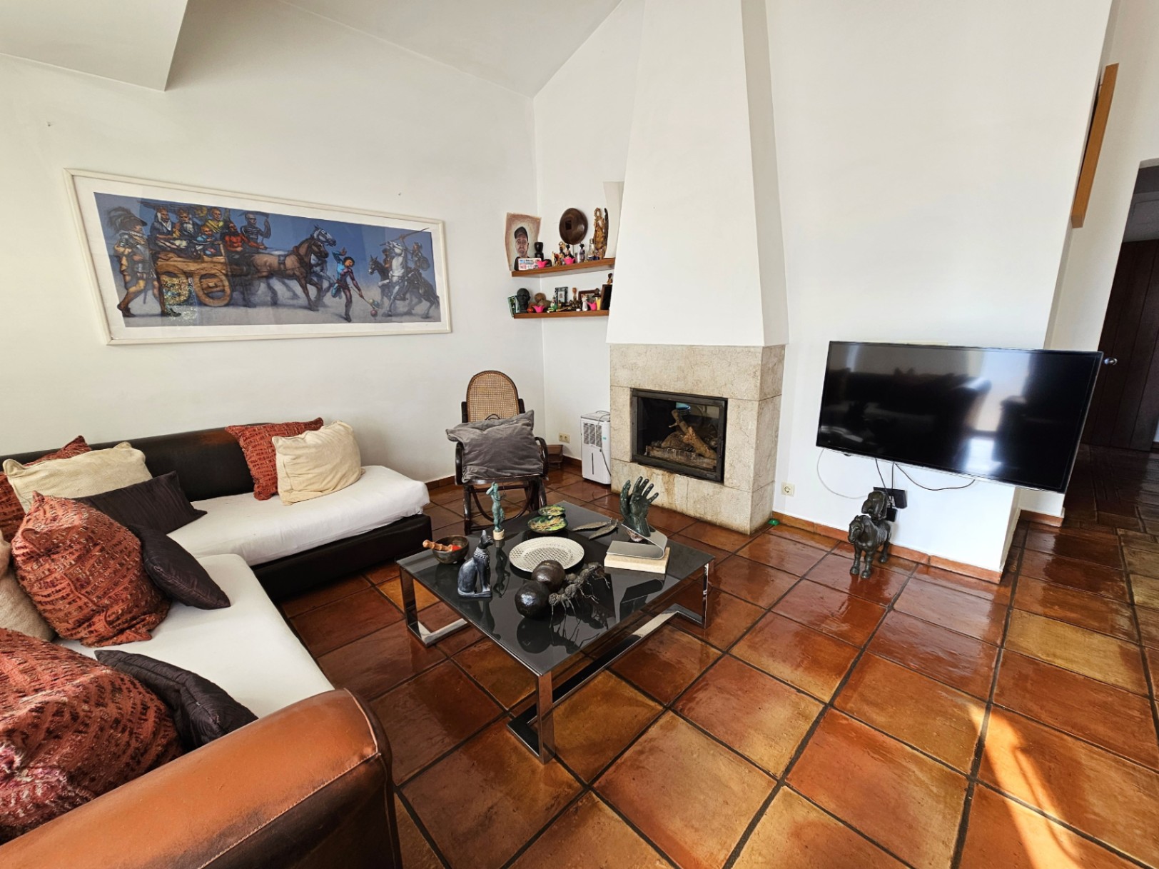 Wohnzimmer mit handgefertigten Tonfliesen und integriertem Steinkamin. Der Raum besticht durch hohe Decken, moderne Möbel und viel natürliches Licht.