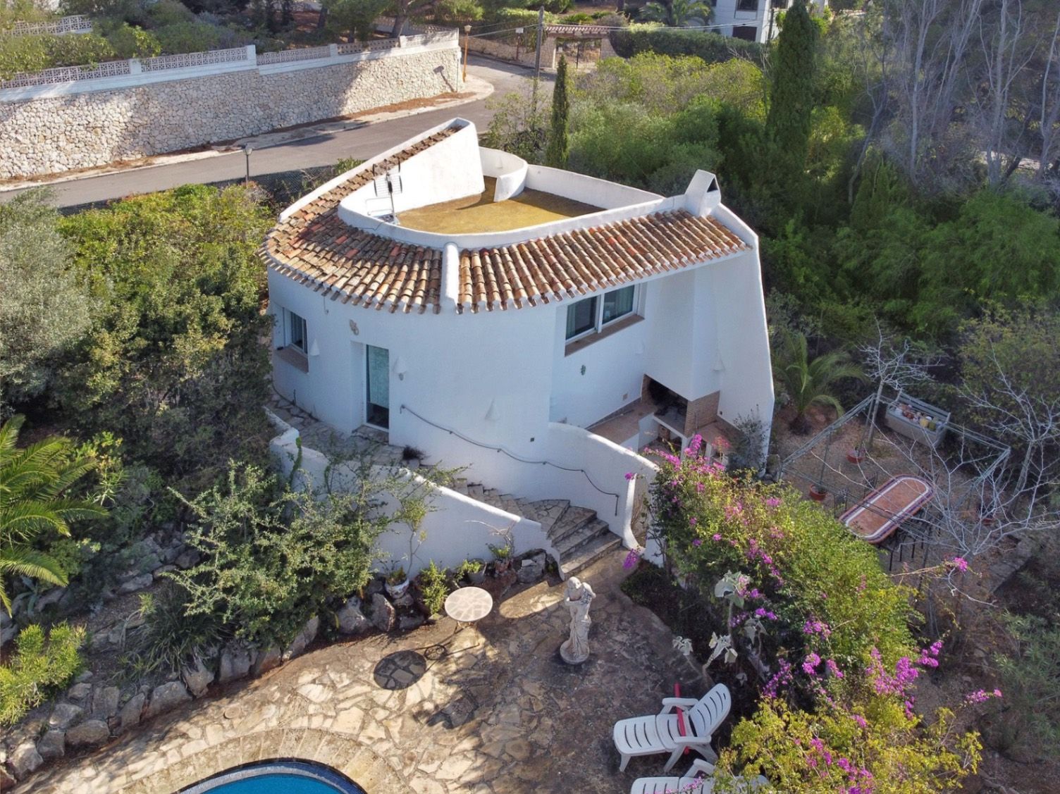 Luftaufnahme der zweiten Villa im mediterranen Stil mit traditionellen Ziegeldächern, Außengrillplatz und Steinterrassen inmitten eines Gartens.
