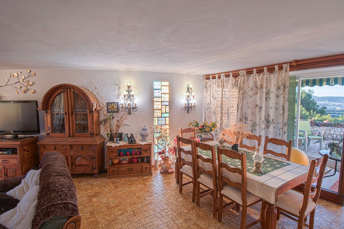 Rustikaler Essbereich mit traditionellen Holzmöbeln, Fliesenboden und großen Glasschiebetüren, die auf eine Terrasse mit weitem Talblick führen.