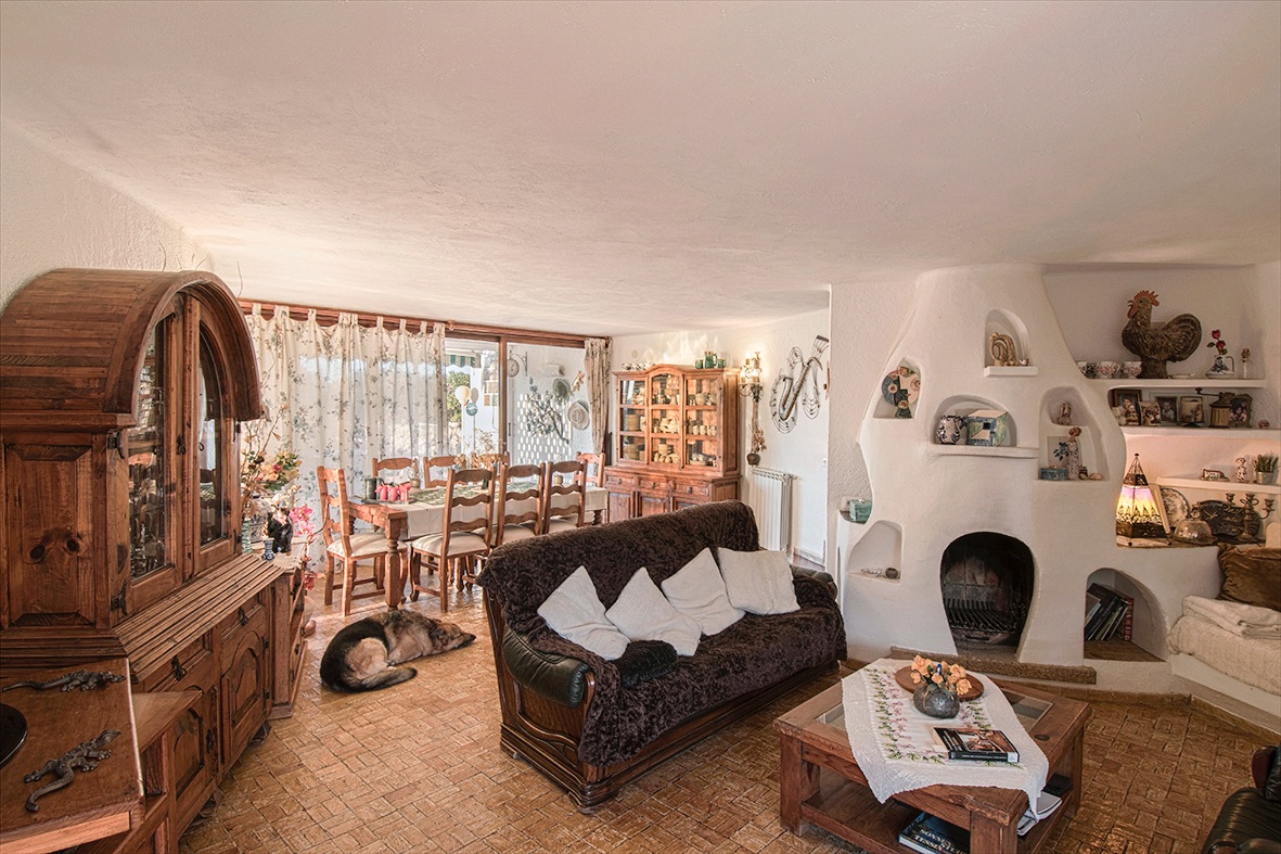 Rustikaler Wohn- und Essbereich mit einem markanten weißen Skulpturkamin, massiven Holzmöbeln und traditionellen Terrakotta-Fliesenböden.