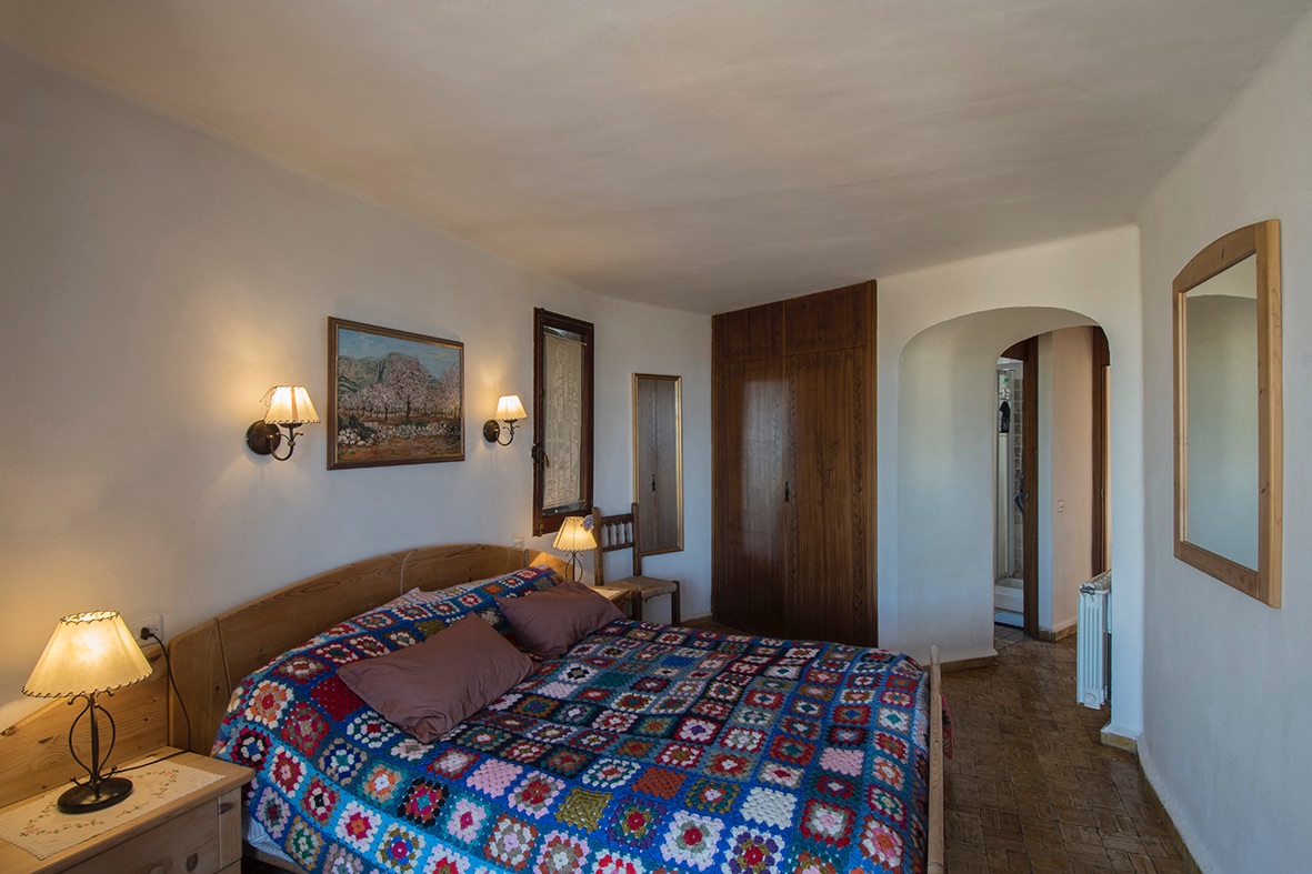 Rustikales Schlafzimmer mit Einbauschränken aus Holz, traditionellem Fliesenboden und einem Rundbogen zum angrenzenden Badezimmer.
