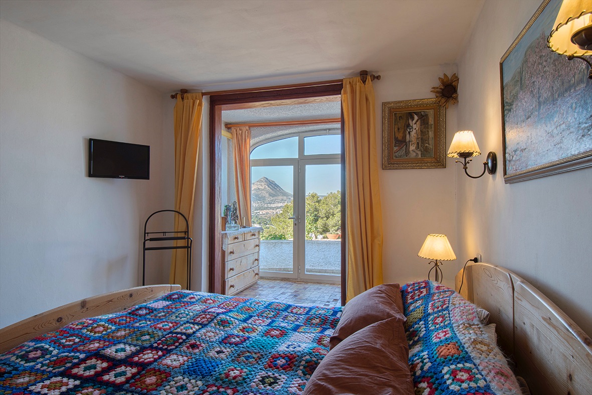 Rustikales Schlafzimmer mit Holzmöbeln und direktem Zugang zu einer Terrasse mit weitem Blick auf die Berge und die umliegende Landschaft.