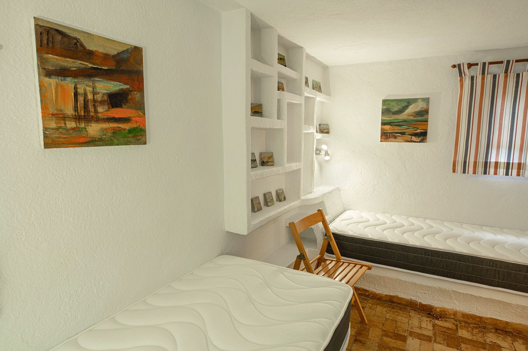 Rustikales Schlafzimmer mit zwei Einzelbetten, integriertem Wandregal und traditionellem Terrakotta-Fliesenboden.