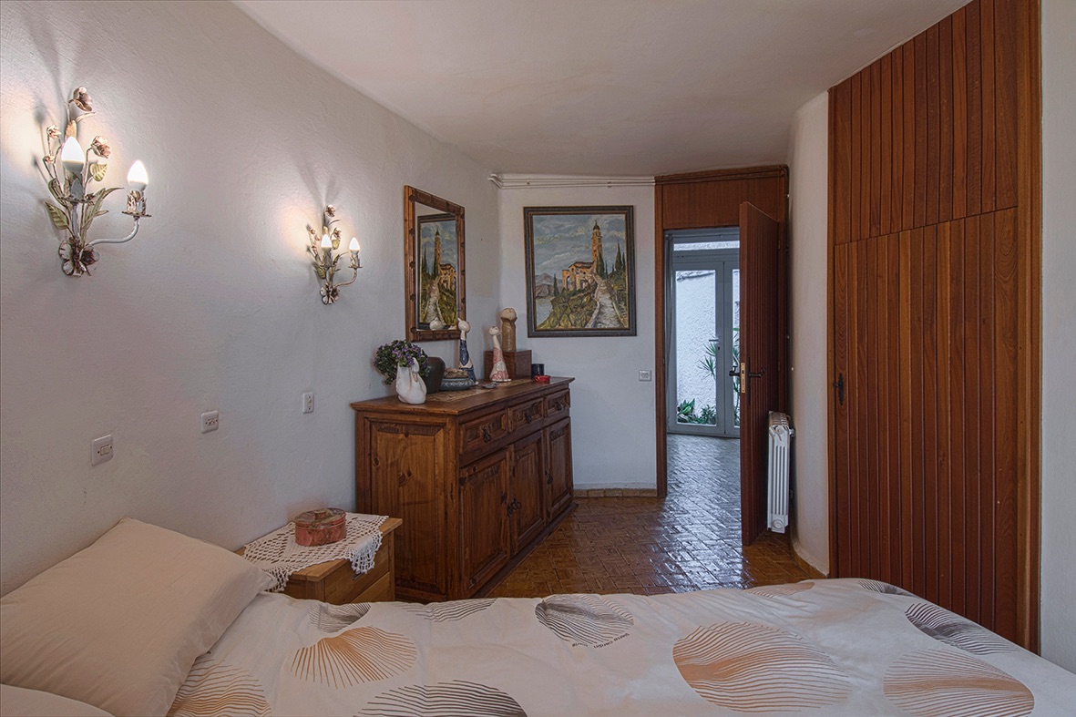 Schlafzimmer mit Einbauschrank aus Holz, rustikaler Kommode und dekorativen Wandleuchten. Ausgestattet mit Fliesenboden und einem Wandheizkörper.