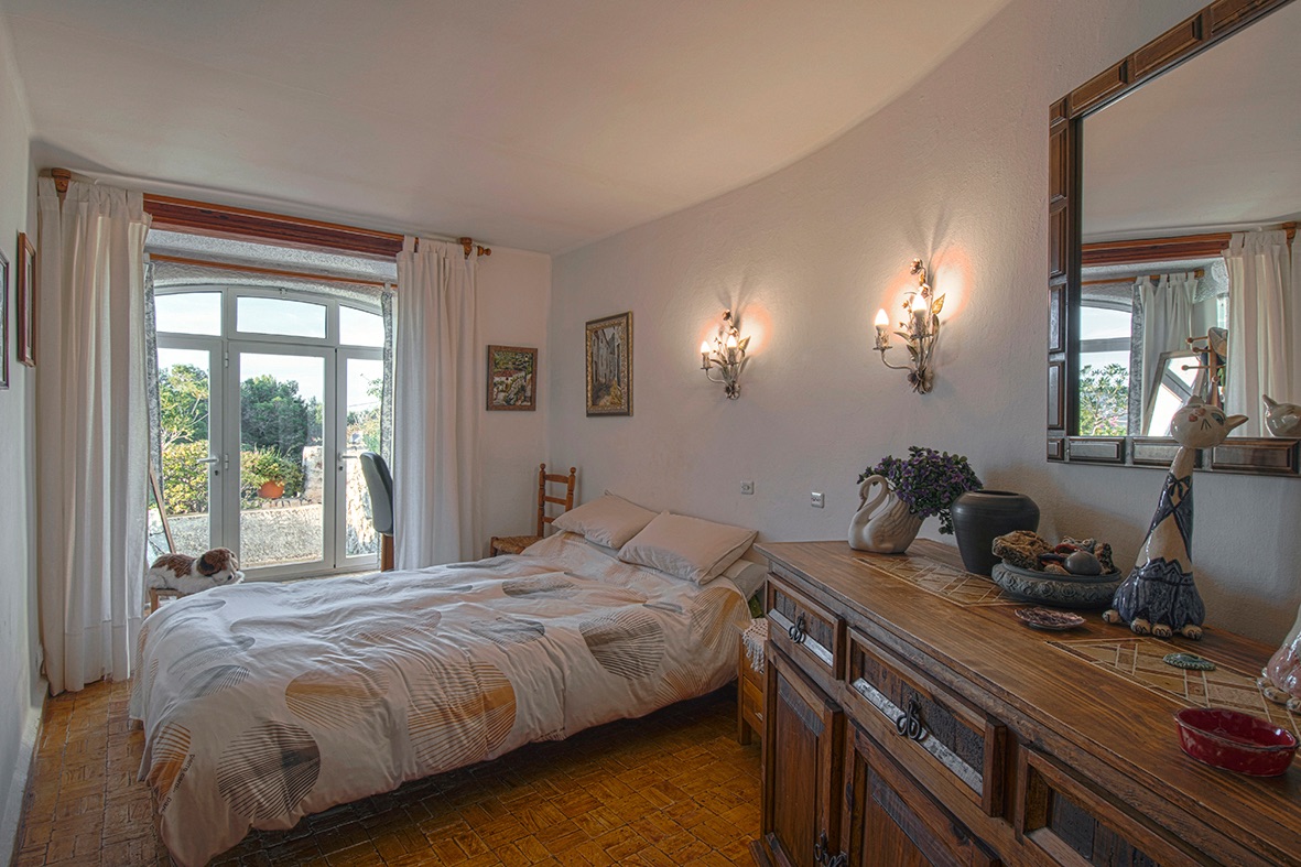Traditionelles Schlafzimmer mit Terrakottaboden, rustikalen Holzmöbeln und einer gewölbten Glastür, die direkten Zugang zum Garten ermöglicht.