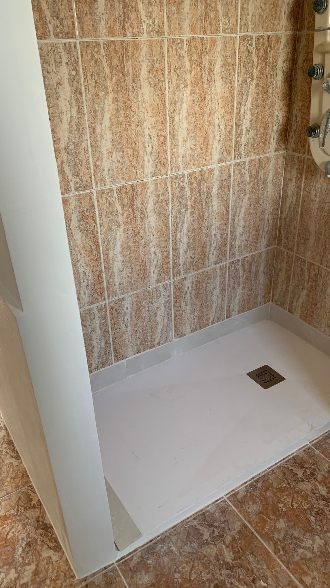 Begehbare Dusche mit weißer Duschwanne, vertikal verlegten Fliesen in Marmoroptik und einer integrierten Hydromassage-Säule.