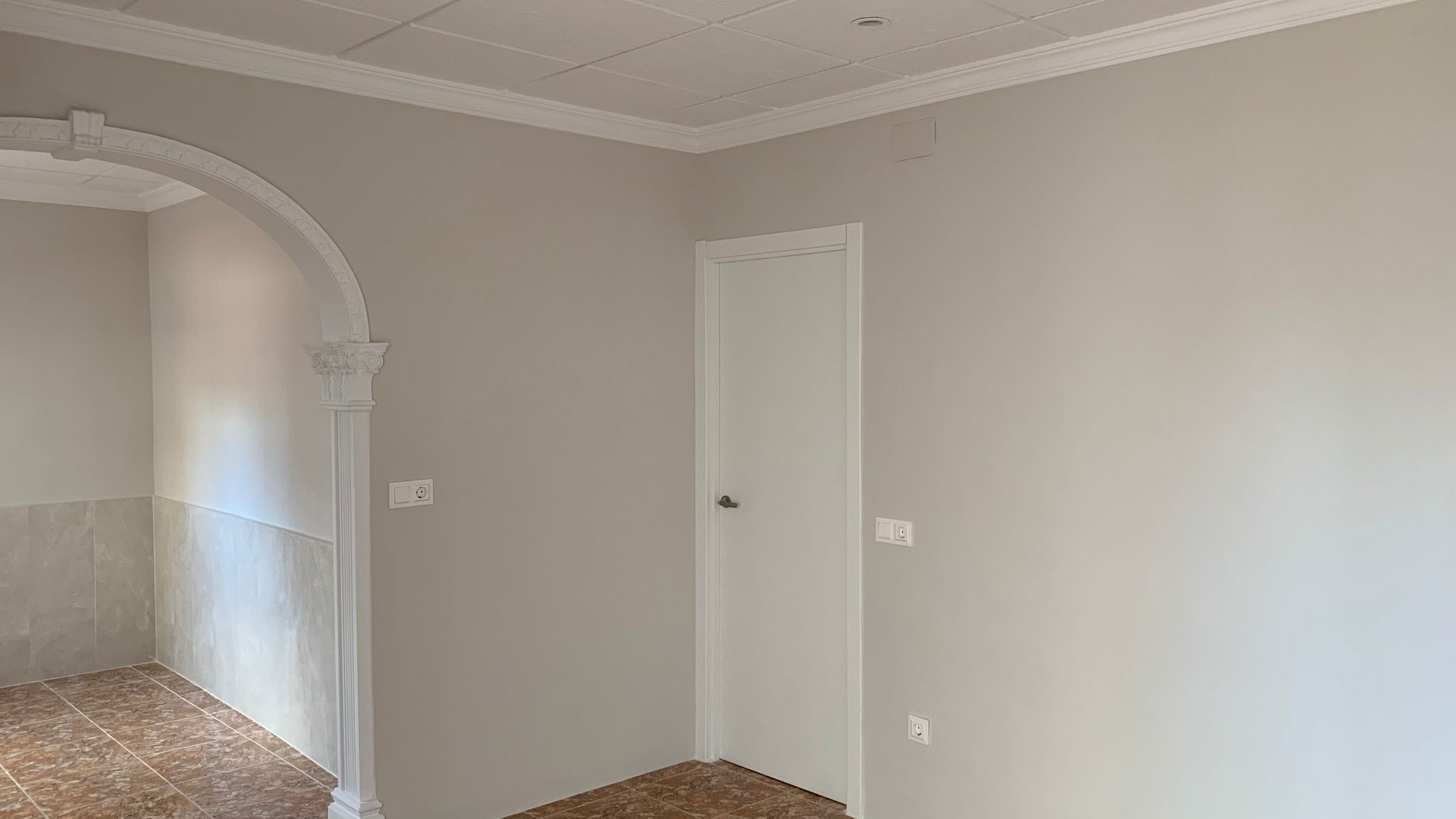 Renovierter Innenraum mit dekorativem klassischem Rundbogen, neutralen Wandfarben, Keramikfliesen und einer Kassettendecke mit eleganten Zierleisten.