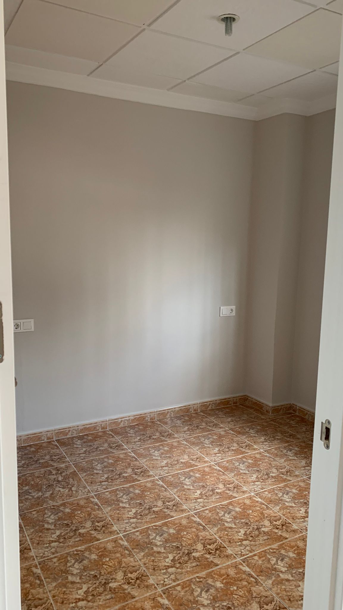 Renovierter Raum mit braun marmorierten Keramikfliesen, hellgrauen Wänden und einer modularen Rasterdecke mit weißen Zierleisten.