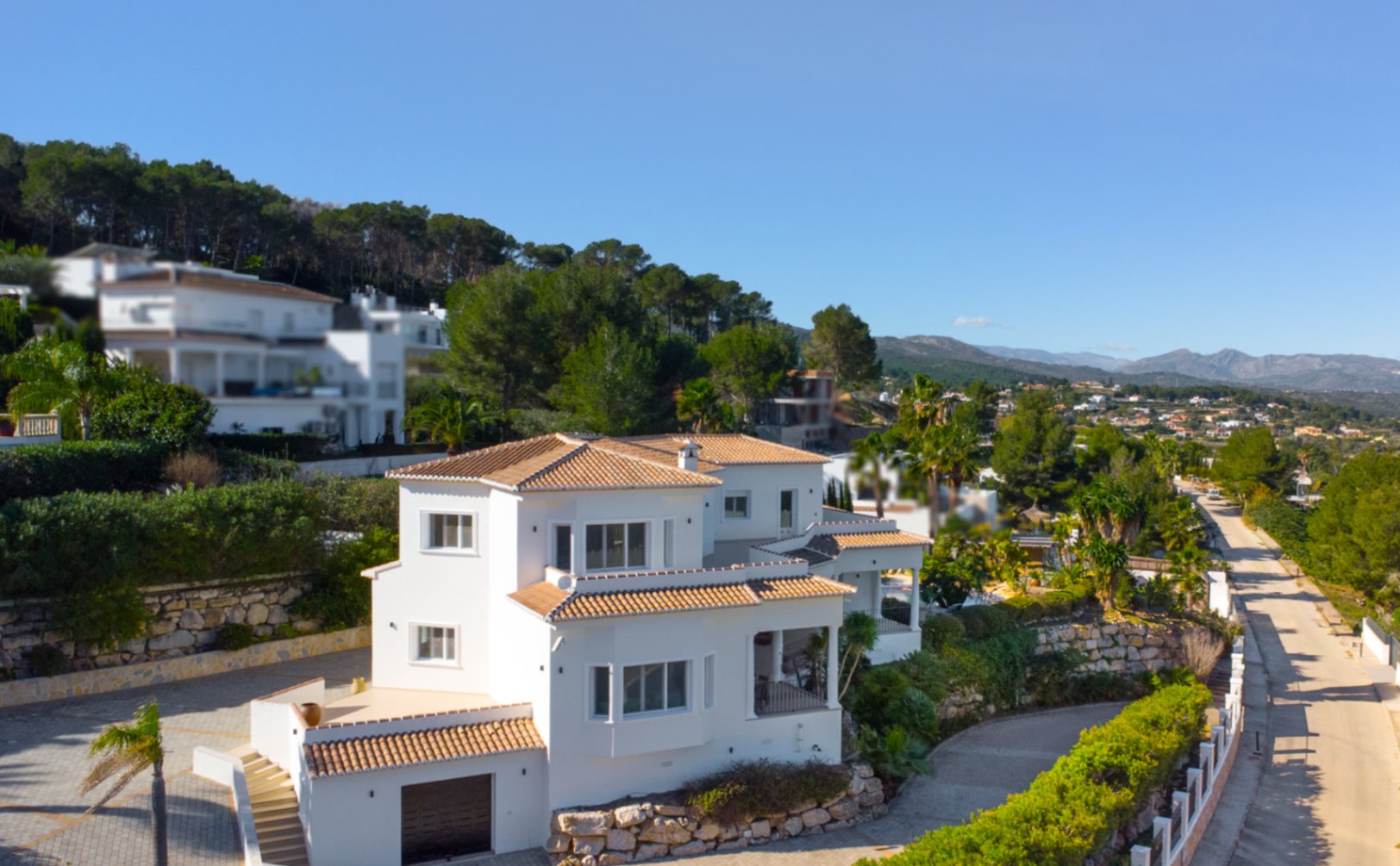Außenansicht der mediterranen Villa mit weißen Fassaden, Terrakottadächern und Natursteinmauern in Hanglage mit weitem Blick auf die umliegende Berglandschaft.