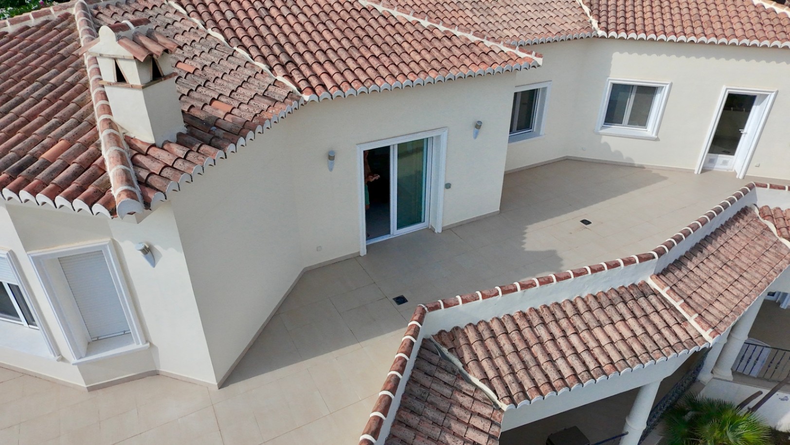 Luftaufnahme der oberen Terrasse und der traditionellen Ziegeldächer mit weißen Fensterrahmen und cremefarbenen Bodenfliesen in versetzter Bauweise.